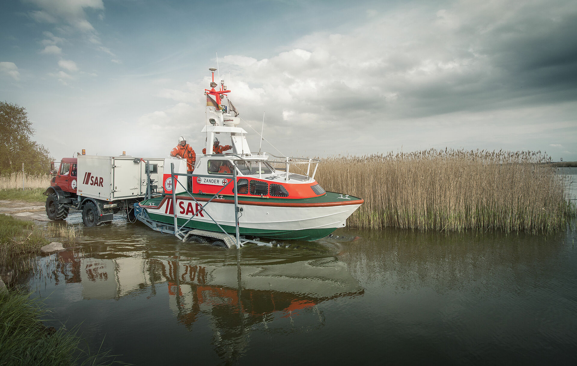 Einsatzfahrzeug schiebt Seenotrettungsboot auf Spezialtrailer ins Wasser