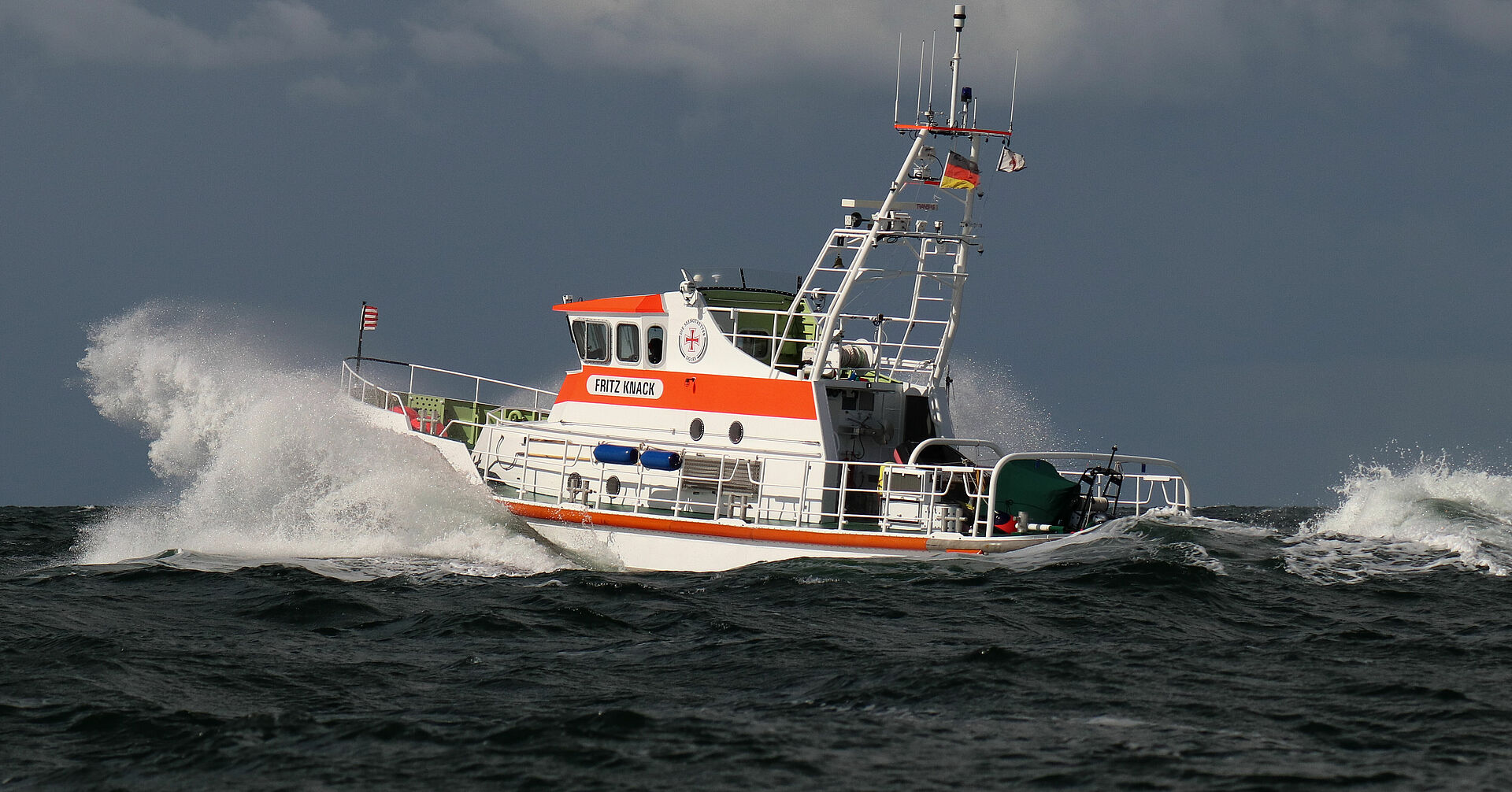 Der Seenotrettungskreuzer FRITZ KNACK fährt durch die Ostsee. Wellen und Gischt schlagen vor dem Bug.