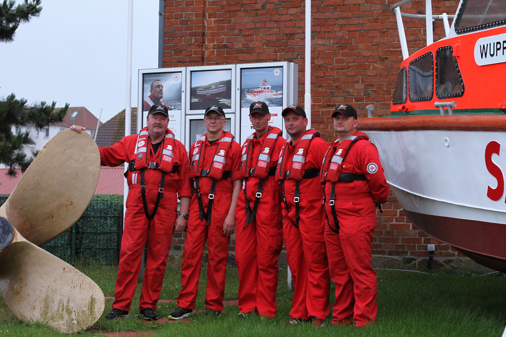 Gruppenfoto einer Seenotretter-Crew zwischen Schiffsschraube und Seenotrettungsboot