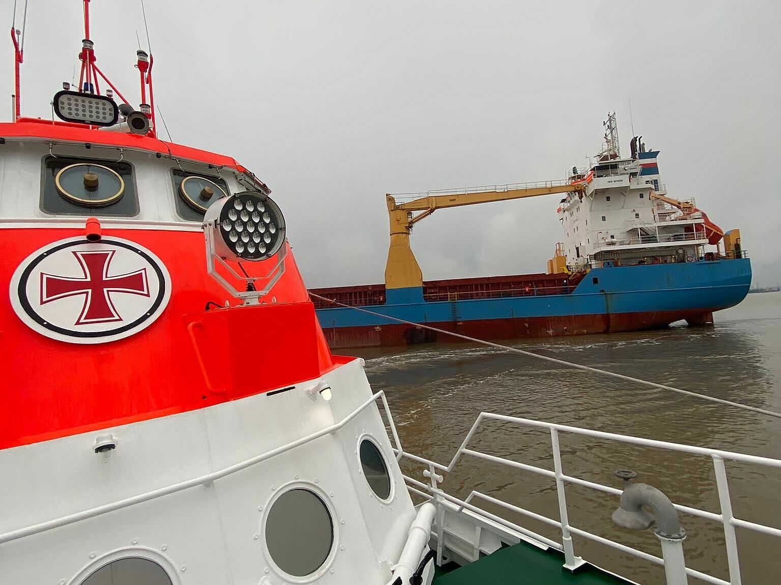 Seenotrettungskreuzer der DGzRS im Vordergrund, Frachtschiff im Hintergrund
