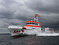 Ein rot-weißer Seenotrettungskreuzer fährt unter wolkenverhangenem Himmel mit hoher Geschwindigkeit über die Ostsee.