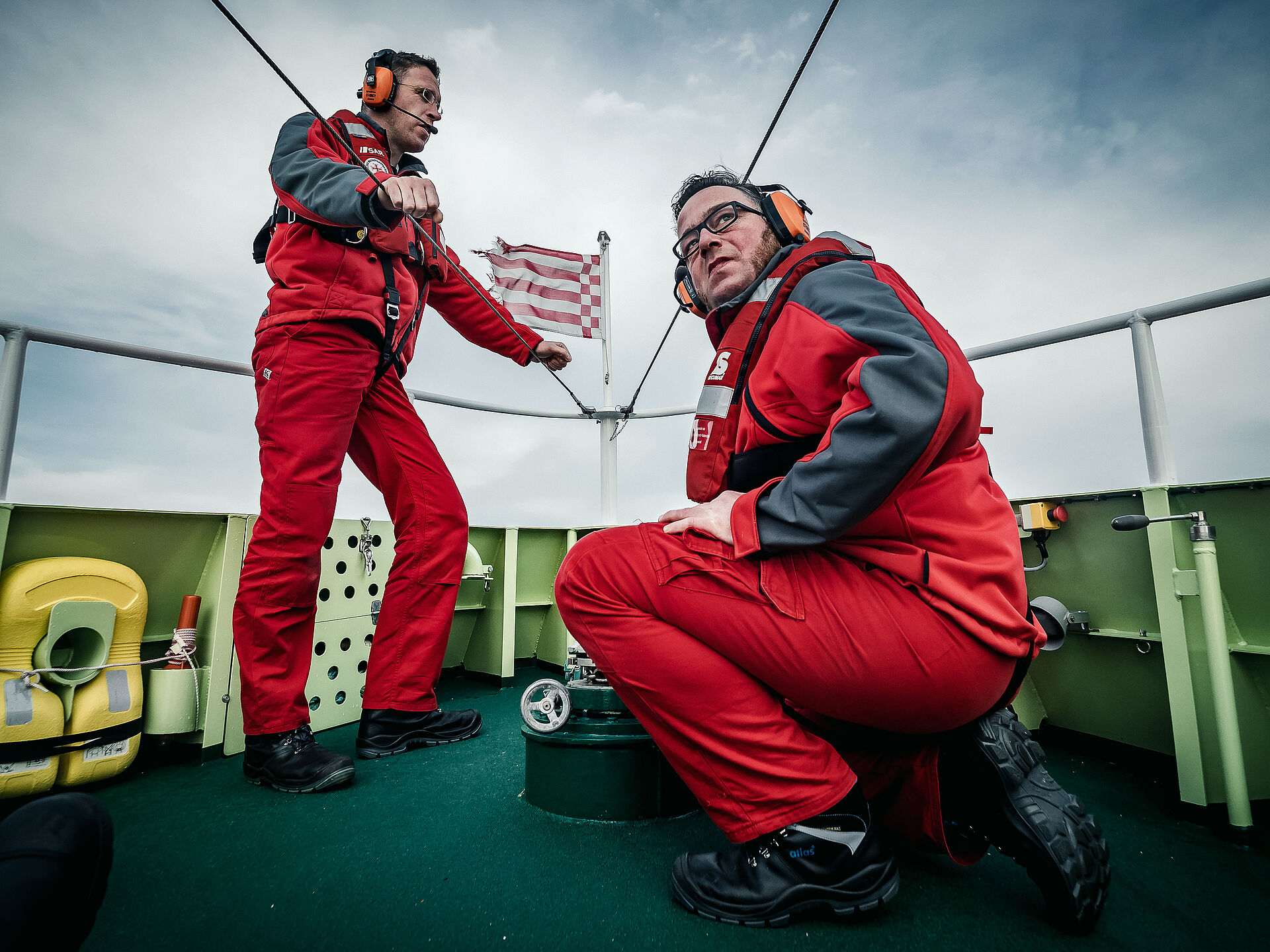 Zwei Seenotretter stehen auf dem Vorschiff eines Seenotrettungskreuzers. Sie tragen ein Headset und schauen konzentriert.