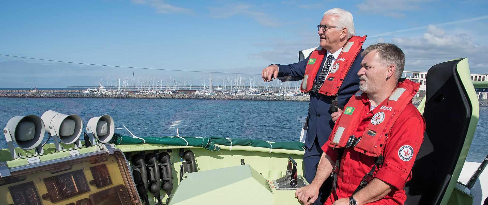 Ein Seenotretter zusammen mit Bundespräsident Frank-Walter Steinmeier bei gutem Wetter an Deck