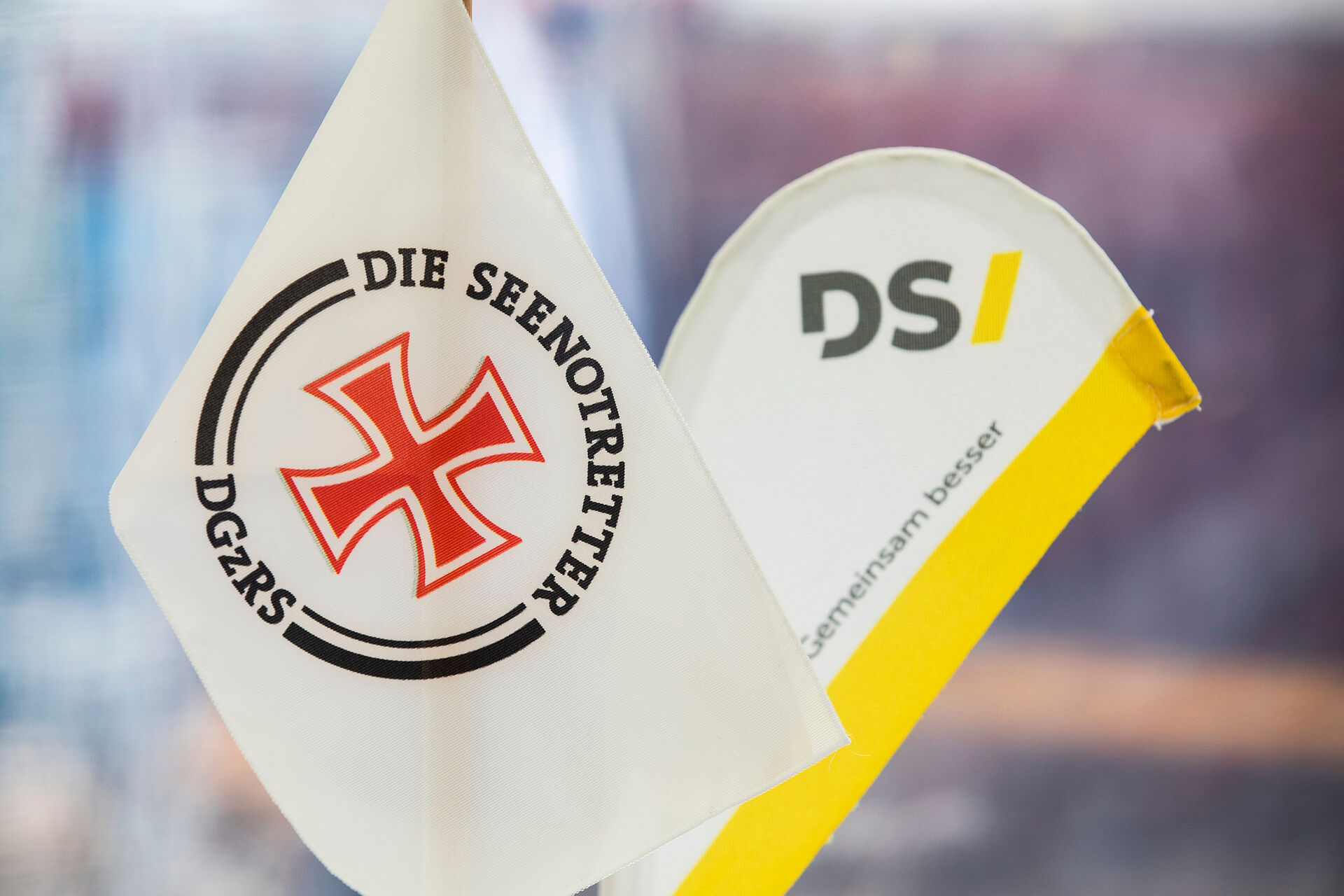 Zwei Tischwimpel, eine mit DGzRS-Logo mit Hansekreuz, eine andere mit gelben DS-Logo der Werft.