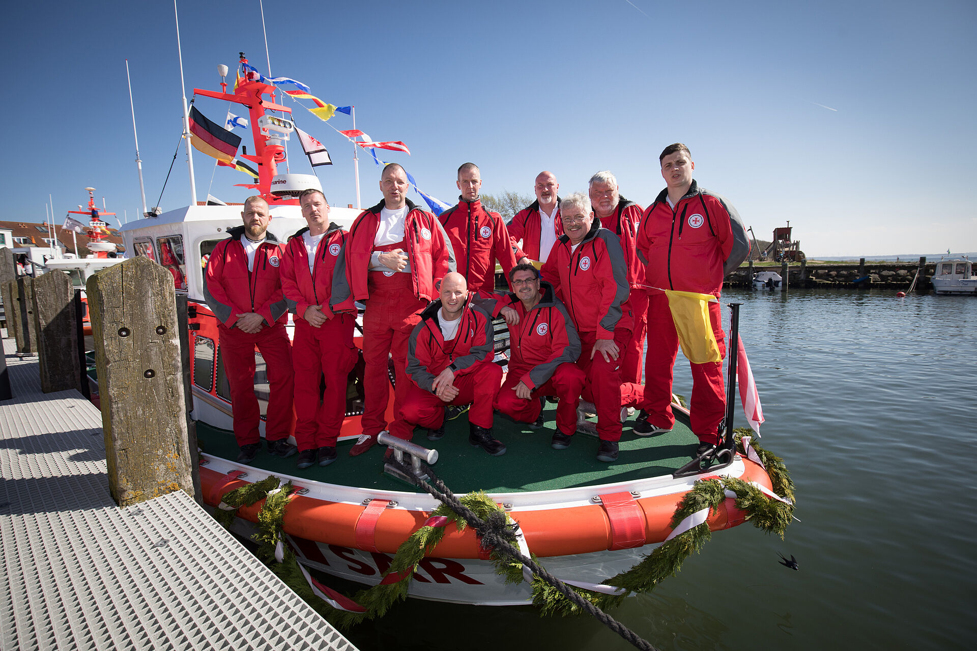 Die Crew der Timmendorfer Seenotretter steht auf dem Vorschiff ihres Seenotrettungsbootes. Es liegt bei Sonnenschein festgemacht im Timmendorfer Hafen auf Poel.