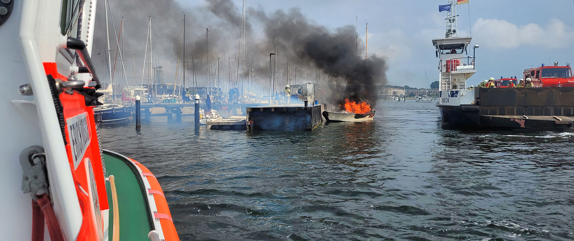 Seenotretter und Feuerwehr löschen vom Land und vom Wasser aus das Feuer auf einem Motorboot