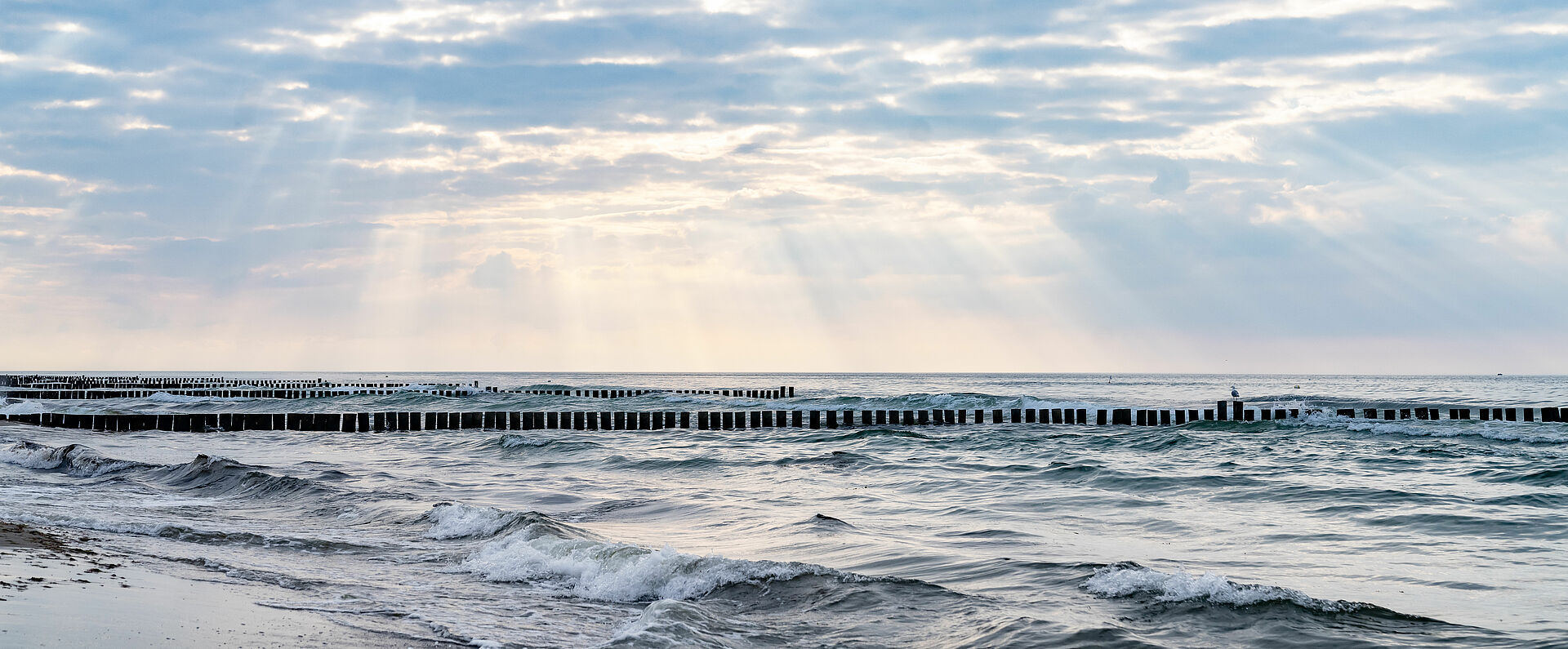 Durch einen dichten Wolkenhimmel dringen Sonnenstrahlen auf das Wasser am Strand vor Kühlungsborn.