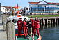 Spendenübergabe auf einem Seenotrettungsboot: Auf diesem stehen vier freiwillige Seenotretter in roter Dienstkleidung. Sie rahmen den NDR-Moderator ein, der ein DGzRS-Sammelschiffchen in den Händen hält. Alle halten einen Daumen hoch.