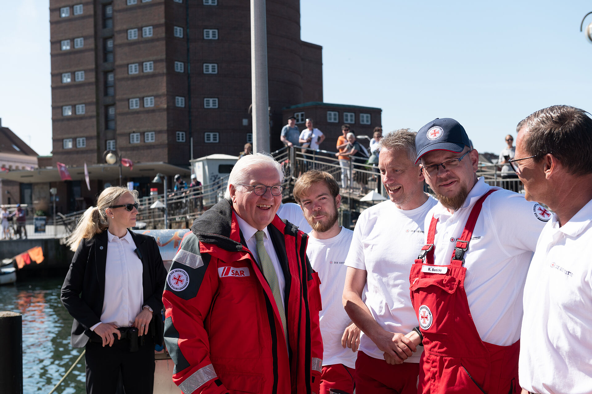 Bundespräsident Frank-Walter Steinmeier steht gemeinsam mit Seenotrettern auf einem Steg und lacht