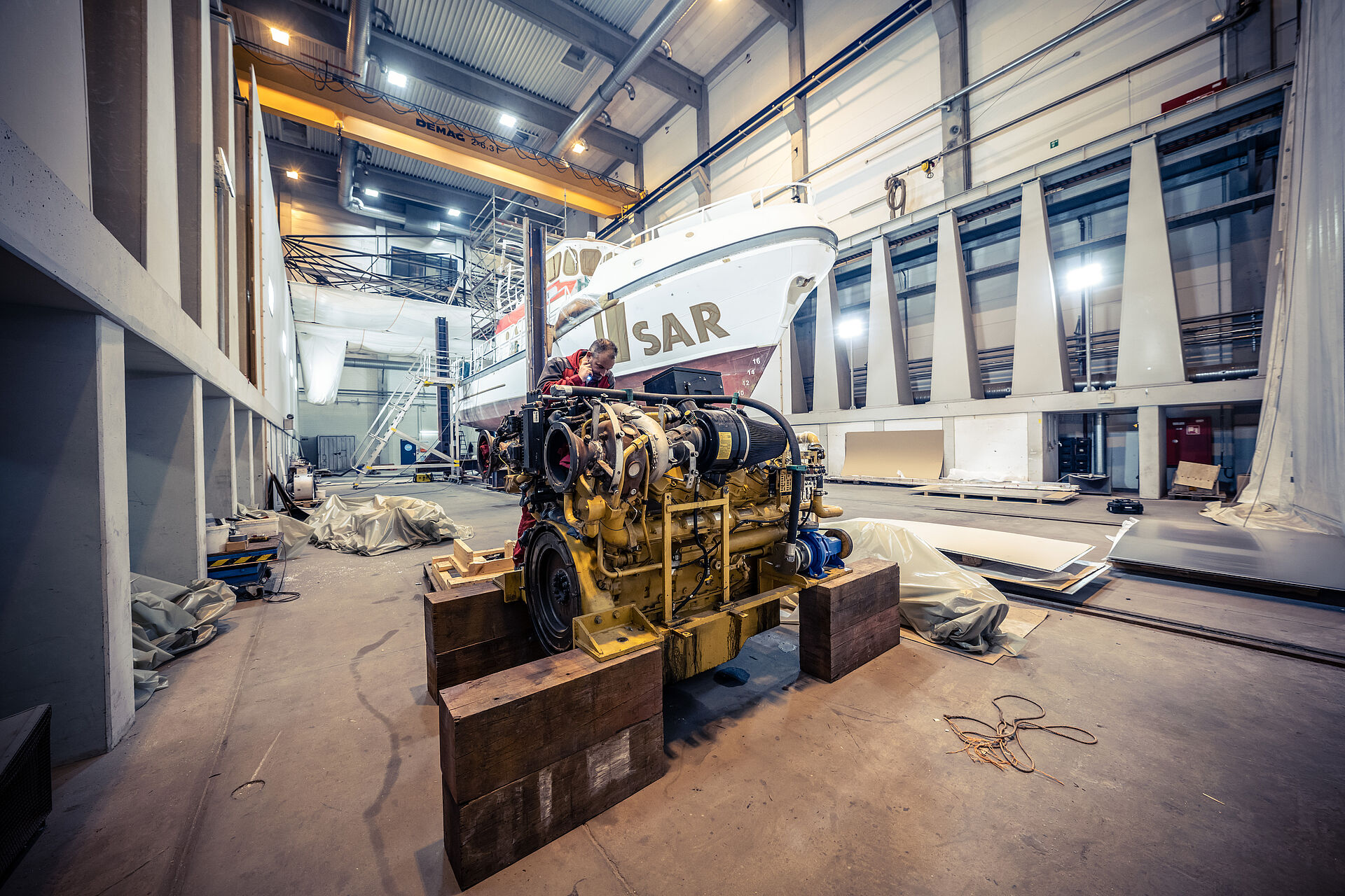 Die Hauptmaschine des Seenotrettungskreuzers wurde bereits ausgebaut und steht vor der EUGEN in der Werfthalle. Vormann Heiko Erdwiens leuchtet mit einer Taschenlampe ins Innere des Motors.