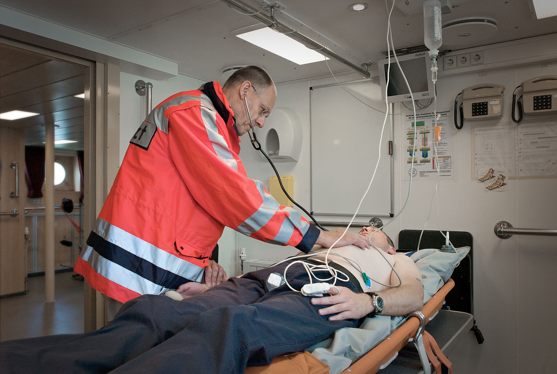 Ein Seenotarzt beugt sich mit Stethoskop über einen Patienten im Bordhospital