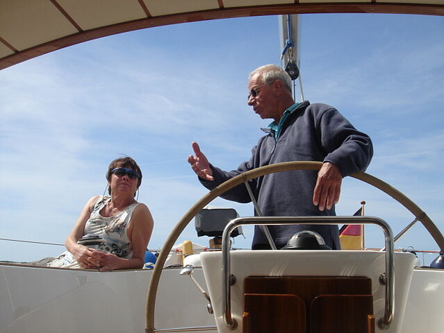 Ein Mann steht am Ruder eines Bootes und unterhält sich mit einer Frau