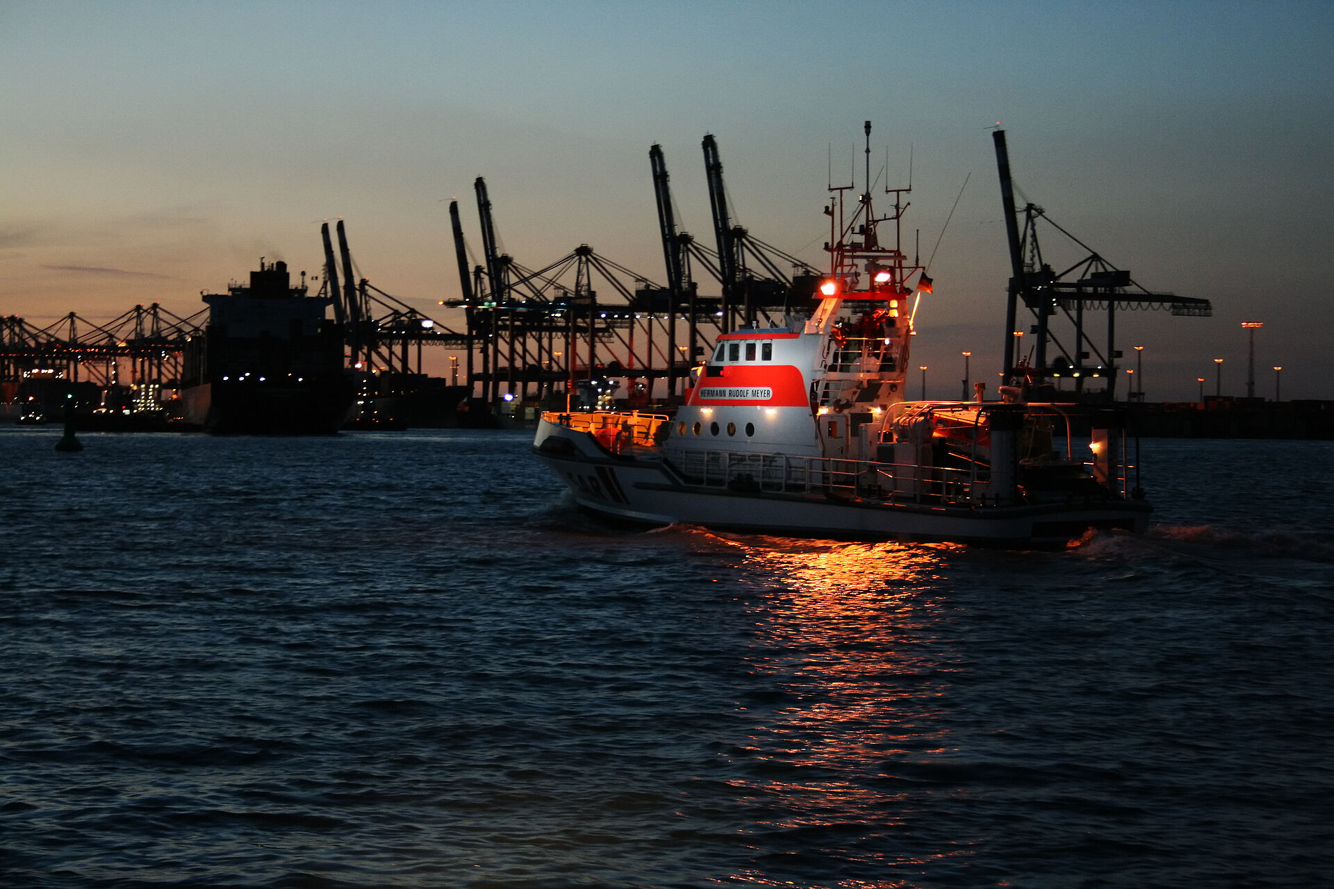Ein Bild von einem Seenotretterkreuzer in der Dämmerung in Front vor einem Hafen