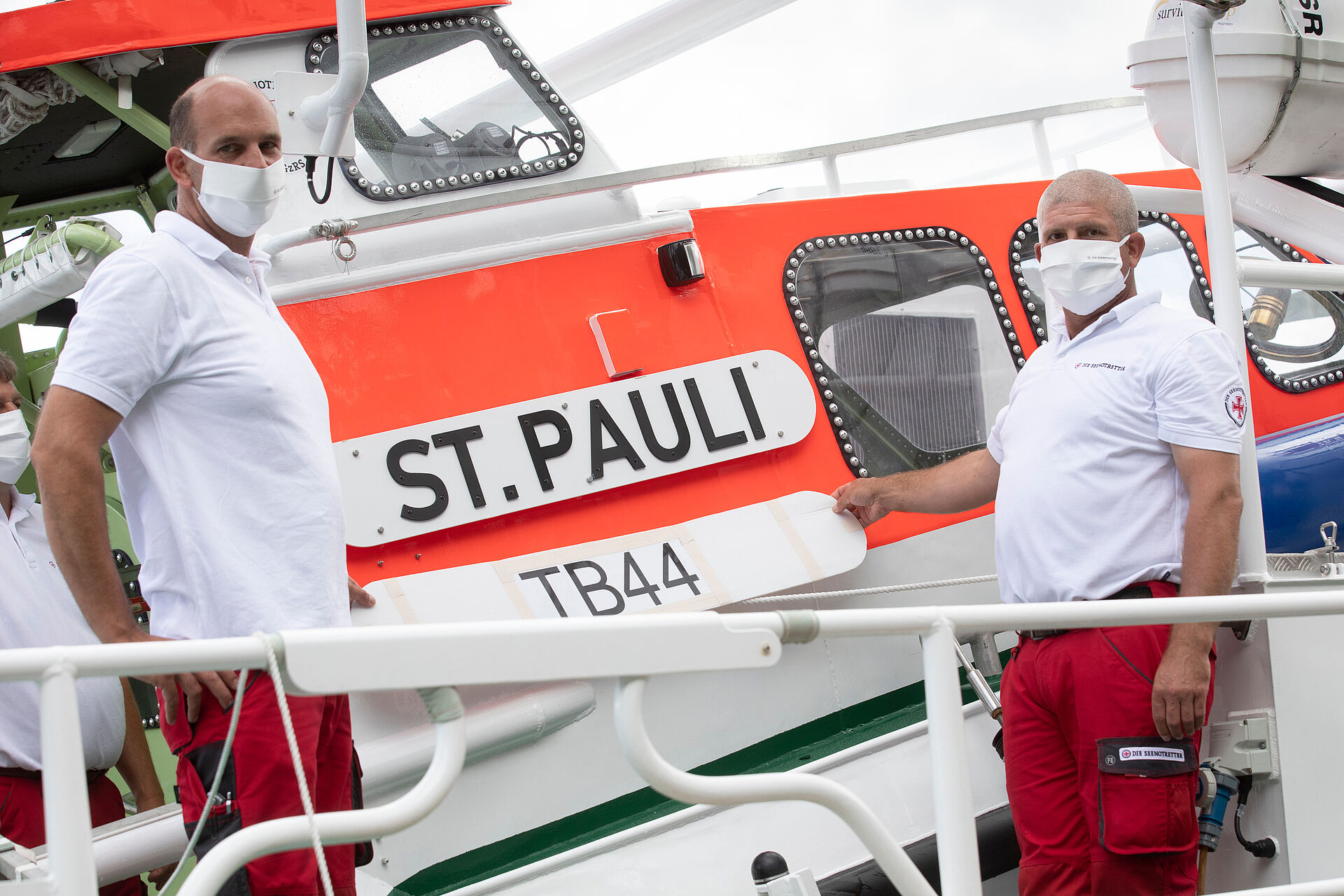 Zwei Seenotretter halten an Deck ihres Seenotrettungskreuzers ein Schild mit der Aufschrift TB44 in den Händen