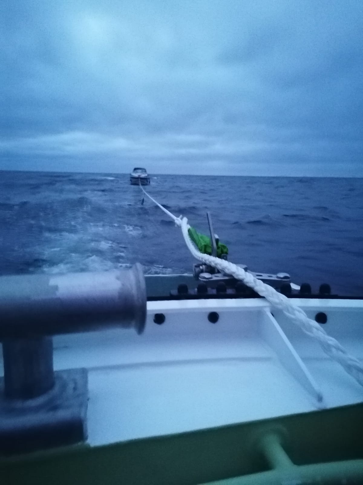 Boot wird an einer Leine nach Rauchentwicklung in der Abenddämmerung von einem Seenotrettungsboot geschleppt