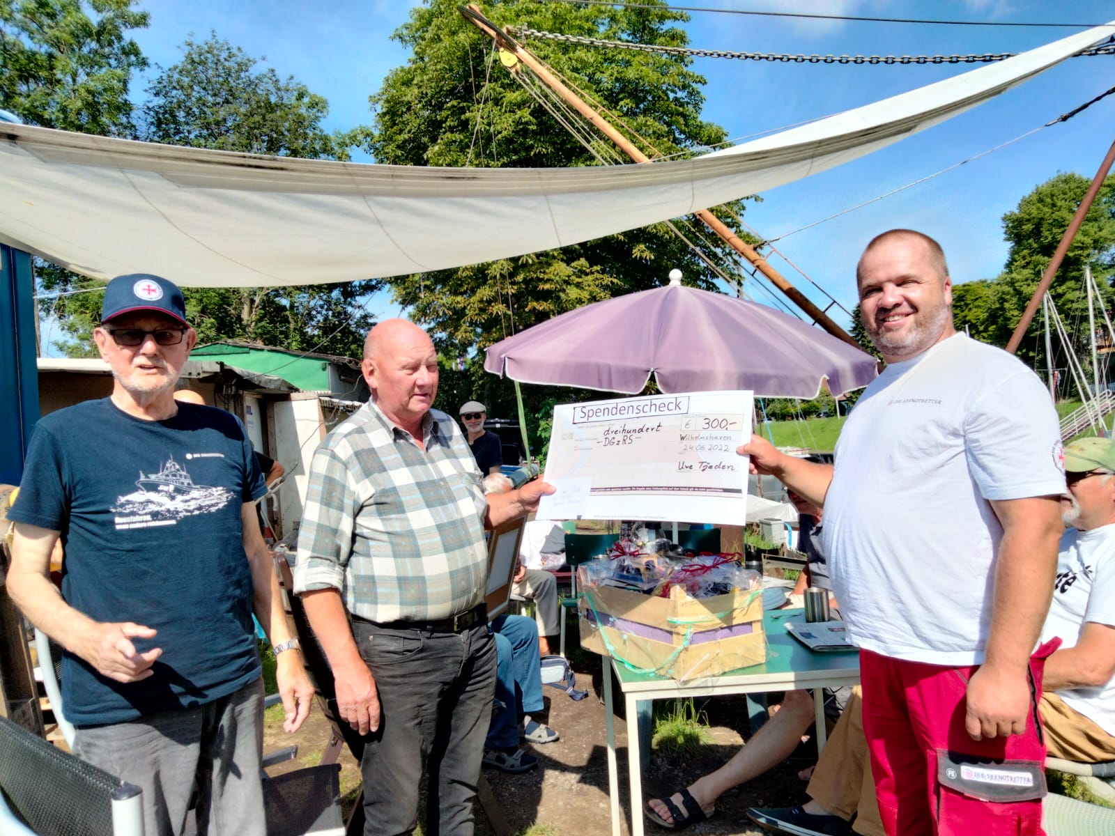 Uwe Tjaden (Mitte) überreicht dem Vormann der Freiwilligen-Station Wilhelmshaven, Stephan von Wecheln (r.), und dem Rettungsmann Günter Thoß einen symbolischen Spendenscheck.