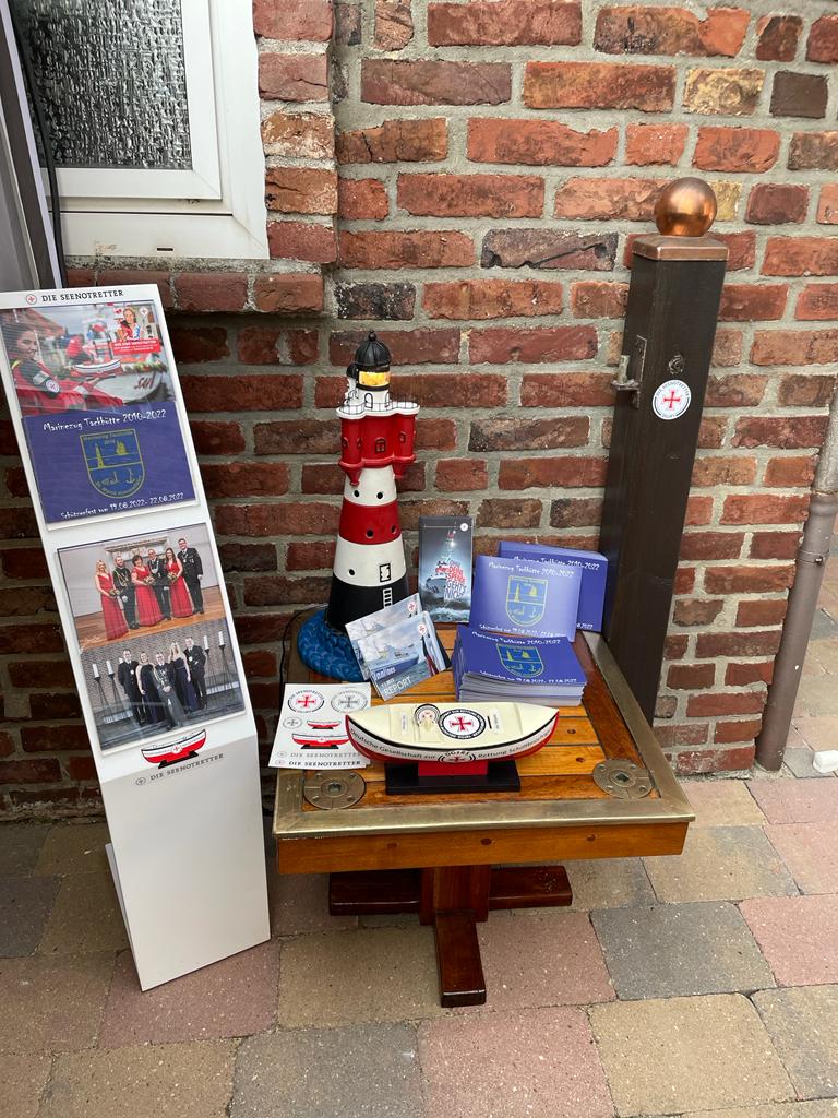 Für die Sammlung des Schützenvereins Mönchengladbach stehen ein Sammelschiffchen der Seenotretter und dazugehörige Flyer auf einem Tisch, dekoriert mit einem Leuchtturm, DGzRS-Aufklebern und Plakaten.