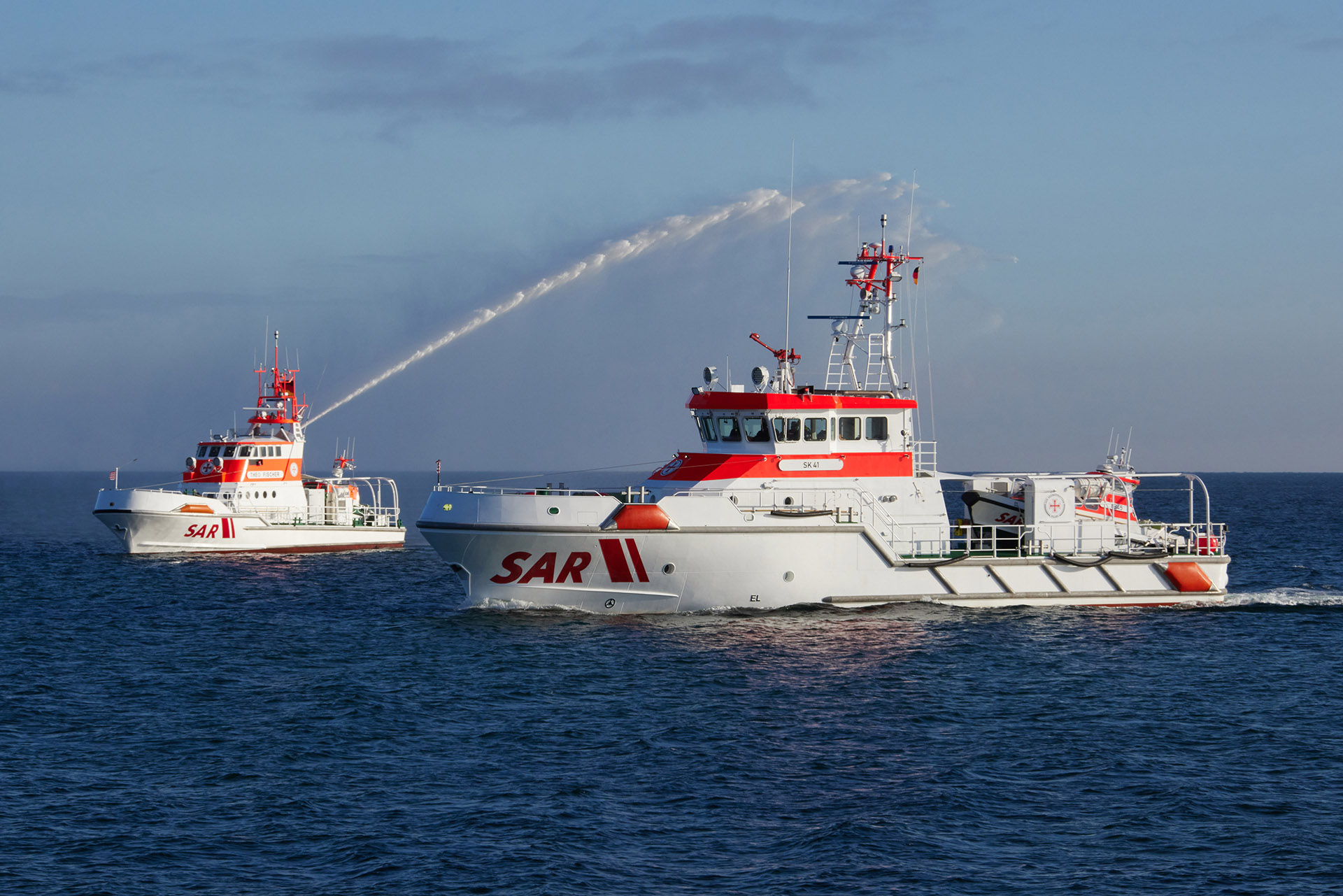 Zwei Schiffe der Seenotretter auf hoher See, während das linke Schiff Wasser in die Luft schießt