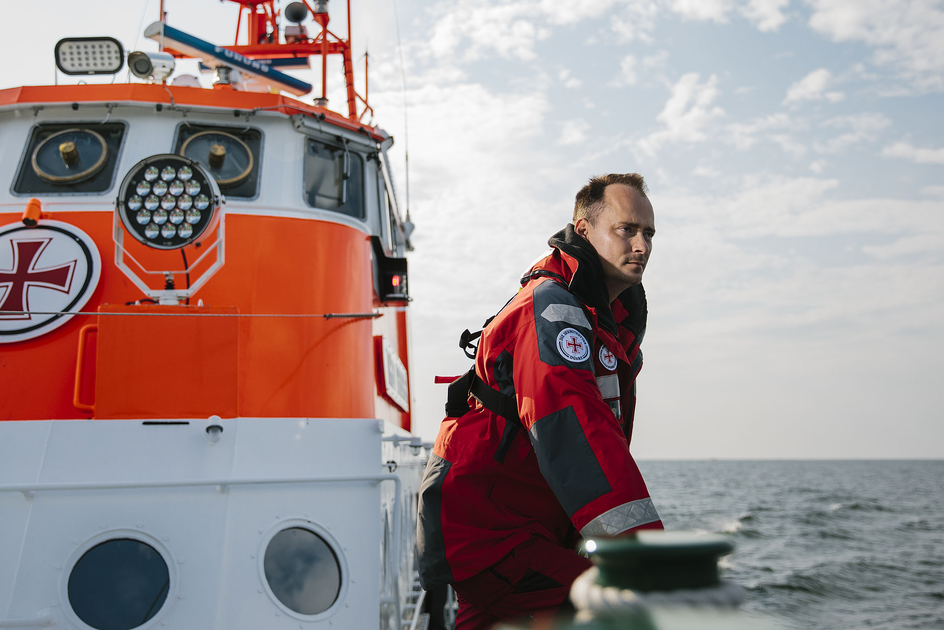 Ein Seenotretter steht aufgestützt an der Reling und schaut in die Ferne